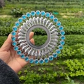 Silver metal round ornament with blue gemstones held in hand against a green field - Bright Silver Light Blue