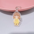 Close-up of cute cartoon girl acrylic keychain with brown pigtails and yellow dress - Orange Backpack Girl (With Lobster Clasp)