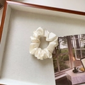 Detailopname van een crème satijnen scrunchie met zachte plooien in een houten tray - Klein / Broken Wit