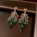 Detailed close-up of vintage gold earrings with emerald green stones and tassels - Gold-Green