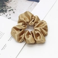 Close-up of champagne gold satin scrunchie with silky texture on a magazine - Tan