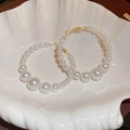 Dettaglio macro di orecchini a cerchio con perle sfumate in un vassoio a conchiglia - Orecchini a Cerchio con Perle Dorate (Perno in Argento)