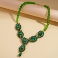 Close-up of vintage necklace with green teardrop crystal pendant and beaded chain detail - Beaded Green Necklace
