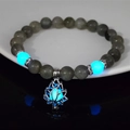 Macro shot of luminous lotus charm bracelet with blue glowing beads on black surface - 8mm Natural Labradorite with Blue Light