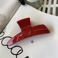 Detail of a glossy bright red large hair claw clip on a white book artistic background - Red