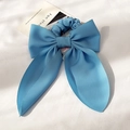 Close-up of a light blue ribbon bow scrunchie on a white textured fabric background - Blue