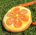 Detail of plush orange slice crossbody bag with adjustable strap on grass background - Orange