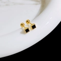 Detail of square gold ear studs with black zircon and screw back on a white ceramic edge - Square / Gold