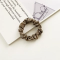 Elastico scrunchie in seta marrone lucida posato su un libro aperto con luce naturale - Marrone Solido Effetto Raso
