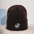 Dunkelbraune Strickmütze mit weißer Rosenstickerei auf einer strukturierten Strohmatte - Einheitsgröße / Weiße Rosenstickerei / Kaffeebraun