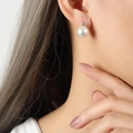 Elegant gold titanium earrings with white pearl and sparkling zircon on model ear - White