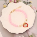 Nahaufnahme des rosa Heishi-Armbands mit rotem Herzanhänger und Strasssteinen auf Tablett - Rosa