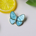 Detalle de broche mariposa azul cielo con base dorada y alas de resina jaspeada - Azul