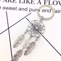 Silver metal dreamcatcher keychain with three feather charms and a white bead on flat white surface - Cream White