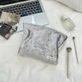 Flat lay of velvet makeup bag with silver gloss finish next to beauty accessories - Gray