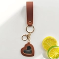 Brown leather heart-shaped mirror keychain with golden metal ring on white background - Warm Coffee