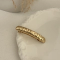 Close-up of golden hammered metal hair clip with textured surface on ceramic plate - Gold-Bar
