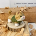 Détail d'une figurine de chat en bois peinte à la main portant un petit gilet vert - Orange Moucheté Avec Vêtements Verts