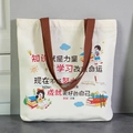Large white canvas tote bag with brown woven handles and colorful student-themed illustrations - Learning Changes Fate