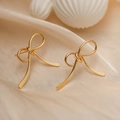 Gros plan de boucles d'oreilles nœuds dorés sur tissu en soie beige avec un éclat doux - Style Long Nœud Mince / Doré