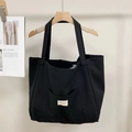 Detail shot of a black canvas tote bag showing the front open pocket and woven brand label - Black