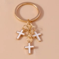 Golden keychain with three white enamel cross pendants on a minimal beige background - White