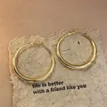 Detailed close-up of minimalist gold hoop earrings on a textured paper background - Gold Medium Polished Hoop Style (53#)