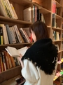 Detail van een zwarte gebreide sjaal met franjes en glitters op een model in een bibliotheek - Eén maat / Zwart