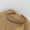 Minimalist slim headband in matte brown leather finish placed on a straw hat background - Brown