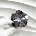 Détail d'une pince à cheveux fleurie en métal sombre brillant tenue par une main - Camélia / Métal canon