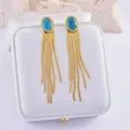 Golden tassel drop earrings with blue oval gemstones on white leather jewelry box - Oval Blue Gemstone