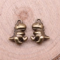 Pair of antique bronze dinosaur pendants for DIY jewelry making on wooden background - Antique Bronze