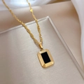 Makro-Detail des goldenen quadratischen Anhängers mit schwarzer Mitte an einer Kordelkette - Gold
