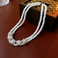 Detail of double-layer pearl necklace with rhinestone flower accents on dark wood surface - White