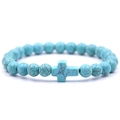 Vista ravvicinata di un bracciale di perle turchesi con croce centrale su sfondo bianco - Howlite Blu