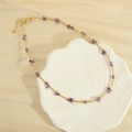 Collana con pietre viola e perle dorate presentata in un piatto a forma di conchiglia - Stile Perlina di Riso (MNE0121)