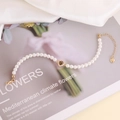 Dettaglio di elegante bracciale di perle con ciondolo a cuore dorato e inserto zircone - Viola