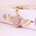 Golden heart wing keychain with colorful rhinestones resting on a book with pink background - White