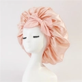 Close-up of pink satin hair sleep cap with large decorative bow on white mannequin head - Medium / Apricot