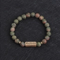 Macro detail of natural unakite stone beads and a gold plate engraved with Powerful - Unakite-Powerful