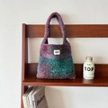 Detail of colorful gradient knit tote bag with brand label on a wooden shelf - M / Red-Green Gradient