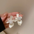 Dettaglio di orecchini a fiore panna con perla tenuti in mano per vedere la misura - Bianco Sporco