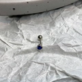 Detail of silver piercing jewelry featuring a pear-shaped dark blue zircon with bead edging - Blue