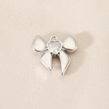 Macro detail of silver bow pendant with heart-shaped cubic zirconia on textured fabric - Heart Zirconia Bow (PJ0262) / Silver