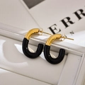 Close-up of modern U-shaped black and gold enamel earrings on a white leather tray - Black
