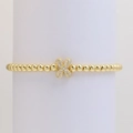 Macro detail of a gold beaded bracelet featuring a shimmering cubic zirconia flower charm - Letter X