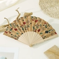 Detailed texture of cork folding fan with red and blue floral patterns on natural wood ribs - Elegant Floral Art