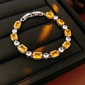Close-up of square yellow gemstone and round zircon bracelet on black leather display - Yellow