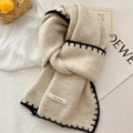 Close-up of beige knitted scarf with black stitching and est move label on white fabric - Off White