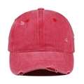 Macro detail of distressed washed red cotton baseball cap showing frayed edges and holes - Watermelon red
